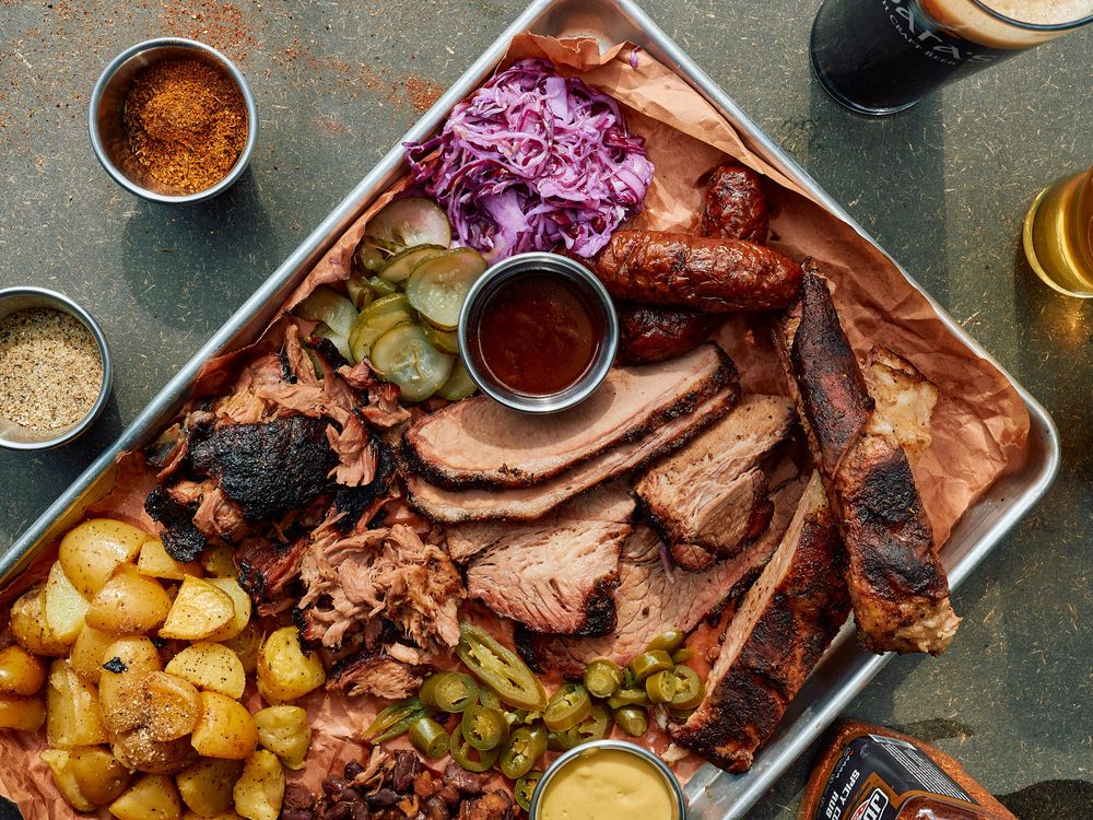 Overhead shot of barbecue platter featuring smoked meats, roasted potatoes and purple cabbage with sauces.