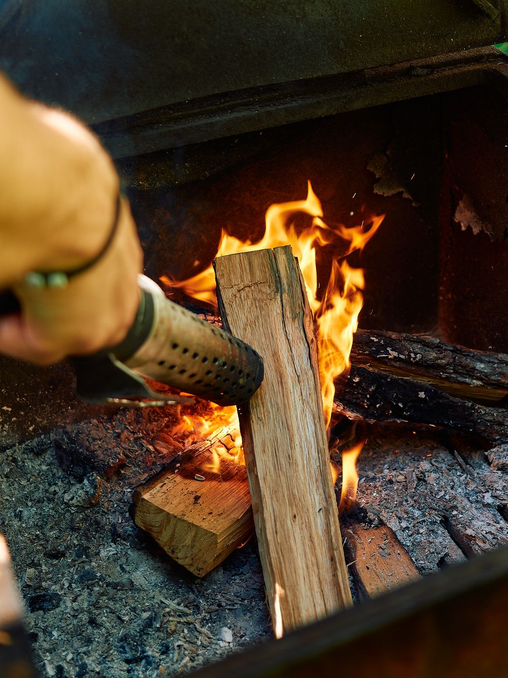 Close-up of a hand using a torch to light firewood in a fireplace.