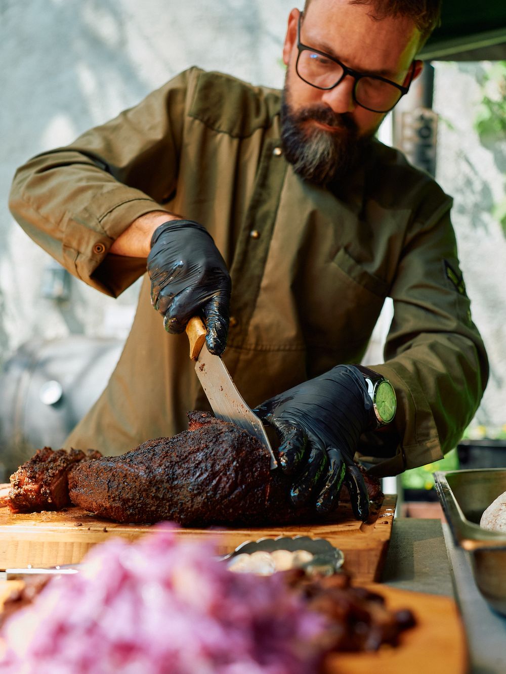 Slicing smoked meat on wooden cutting board with black gloves.
