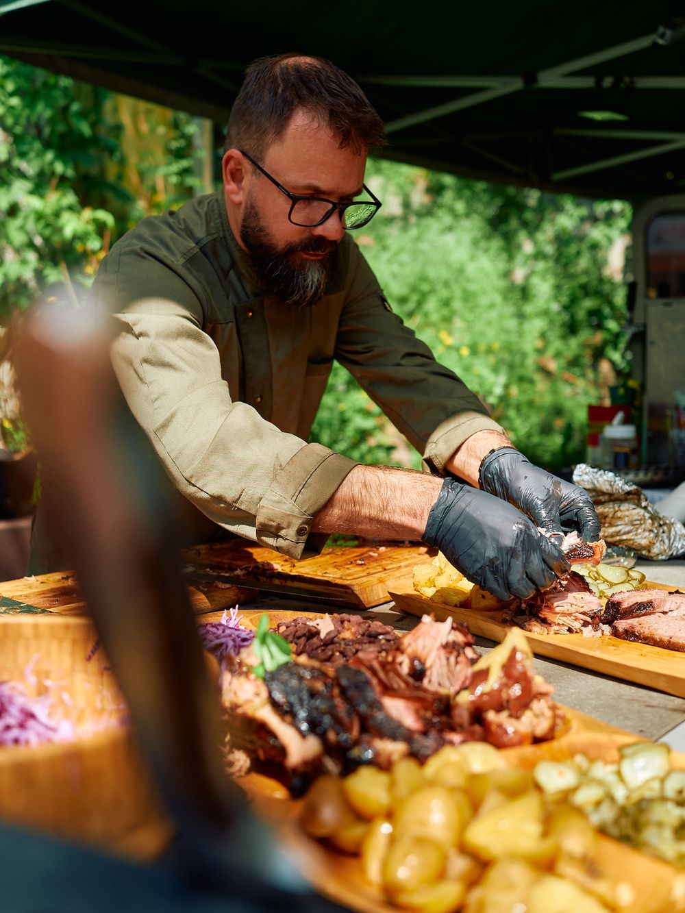 BBQ chef preparing various smoked meats and sides at outdoor station.