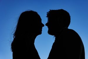 Silhouette of a couple against a bright blue sky in an intimate moment.