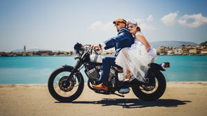 Newlyweds pose on a vintage motorcycle against a beautiful coastal backdrop.