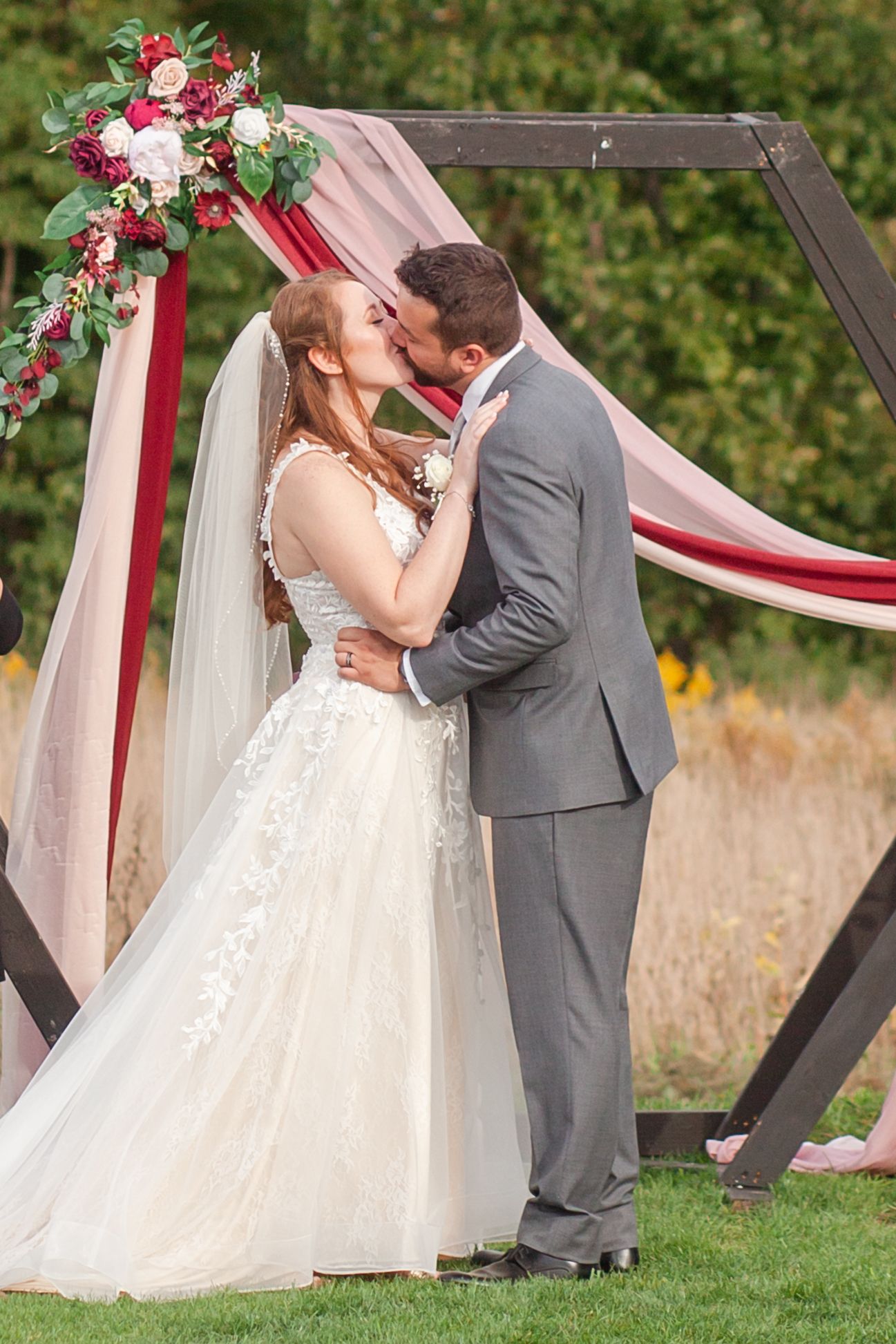 A romantic moment under a white and burgundy decorated wedding arch adorned with fresh flowers.