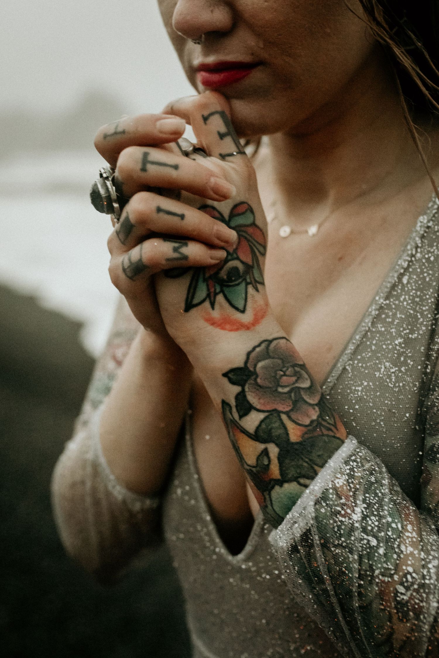 Close-up of bride's tattooed hands and chest in sparkly wedding gown.