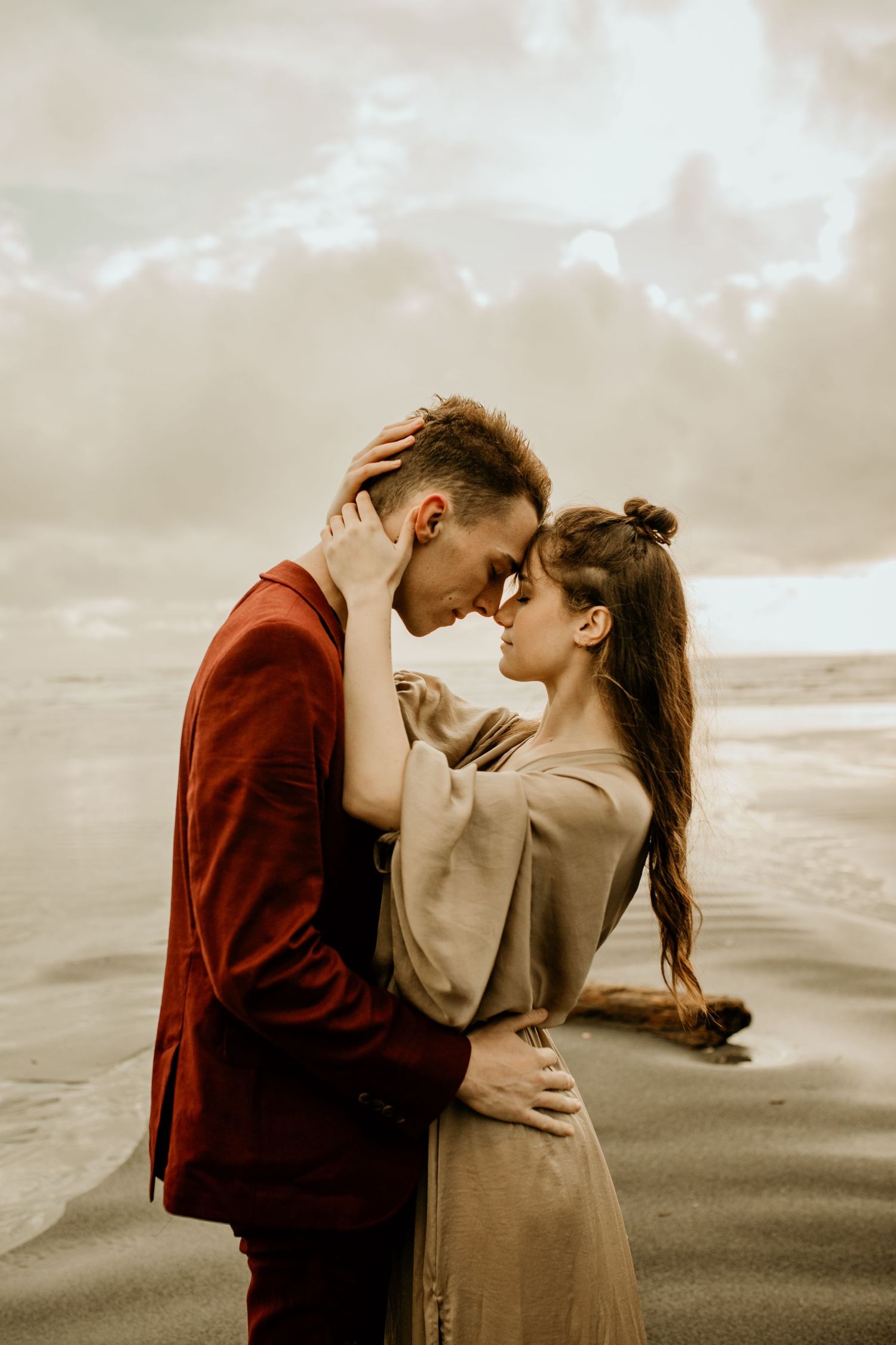 Couple sharing a tender forehead-to-forehead embrace on a sandy beach at sunset.