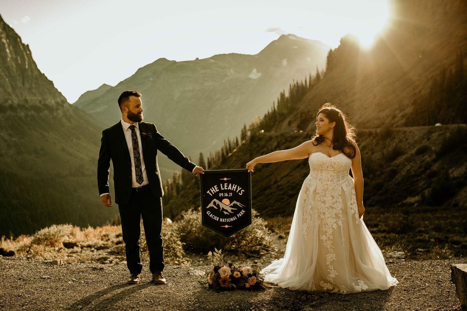 Bride and groom hold a banner at golden hour with stunning mountain backdrop during elopement.
