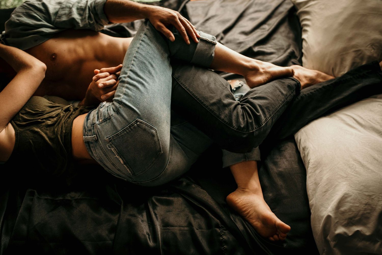 Romantic couple cuddling together on gray bedding, wearing casual jeans in a cozy bedroom setting.