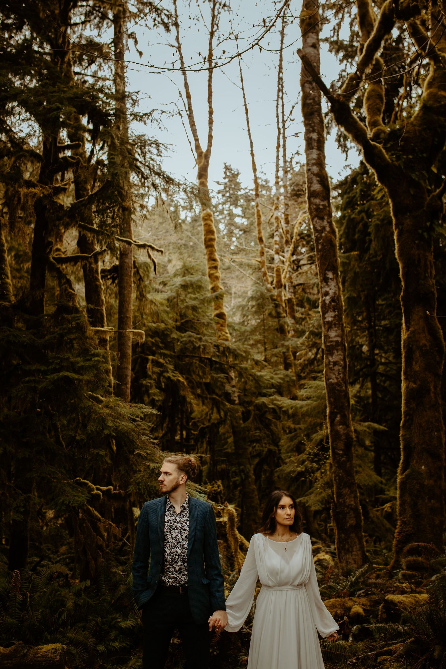 Couple holds hands in lush mossy Pacific Northwest forest during elopement.
