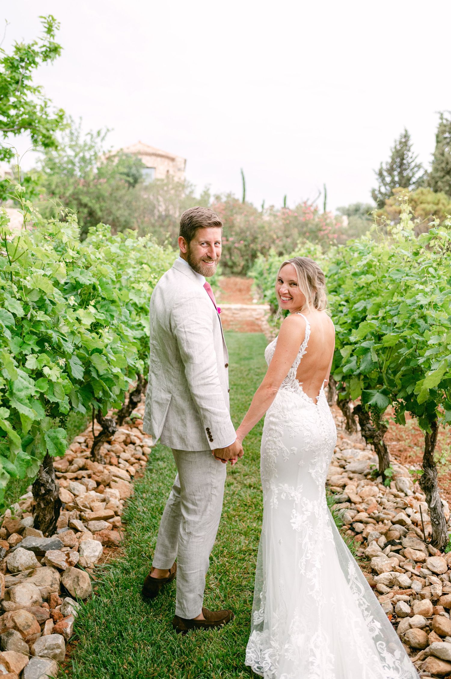 A romantic wedding photograph taken in a vineyard with lush green vines and stone terracing.
