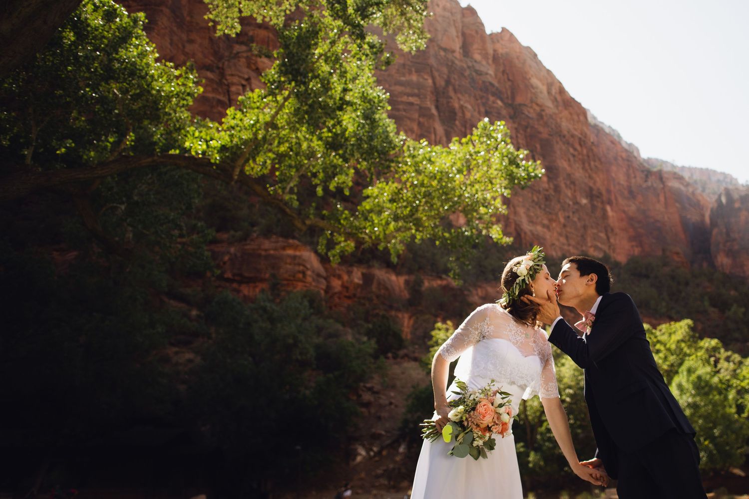 Couple kissing at Zion National Park by a red canyon wall.