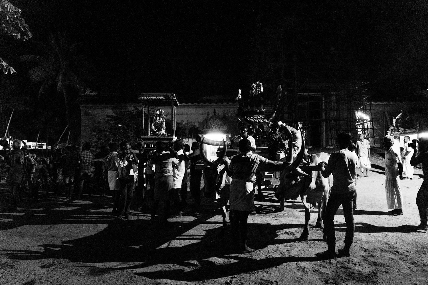 A black and white night scene showing people gathering around street food vendors with bright lights illuminating the area.