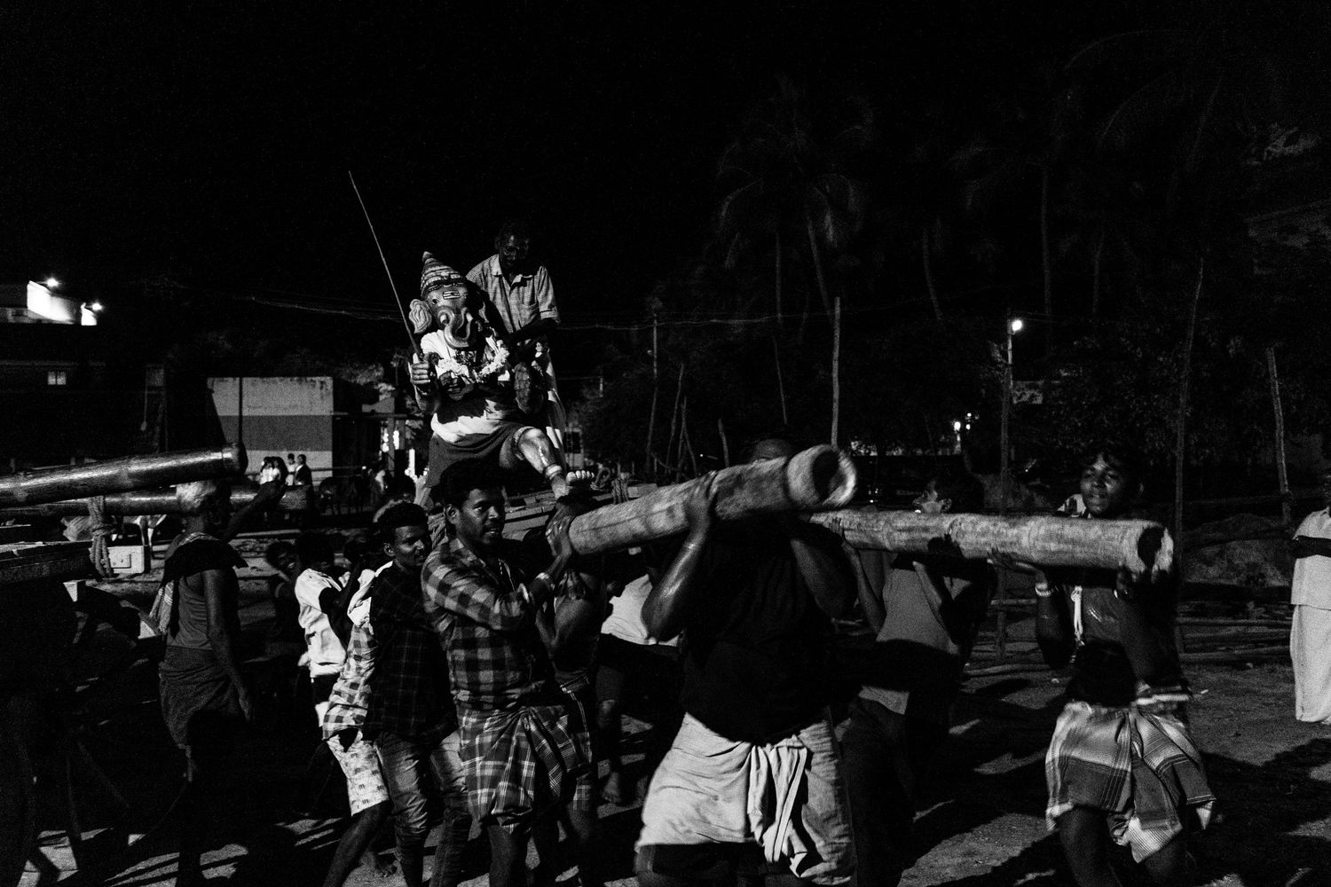 Group carrying large ceremonial logs during a traditional Hawaiian nighttime performance.