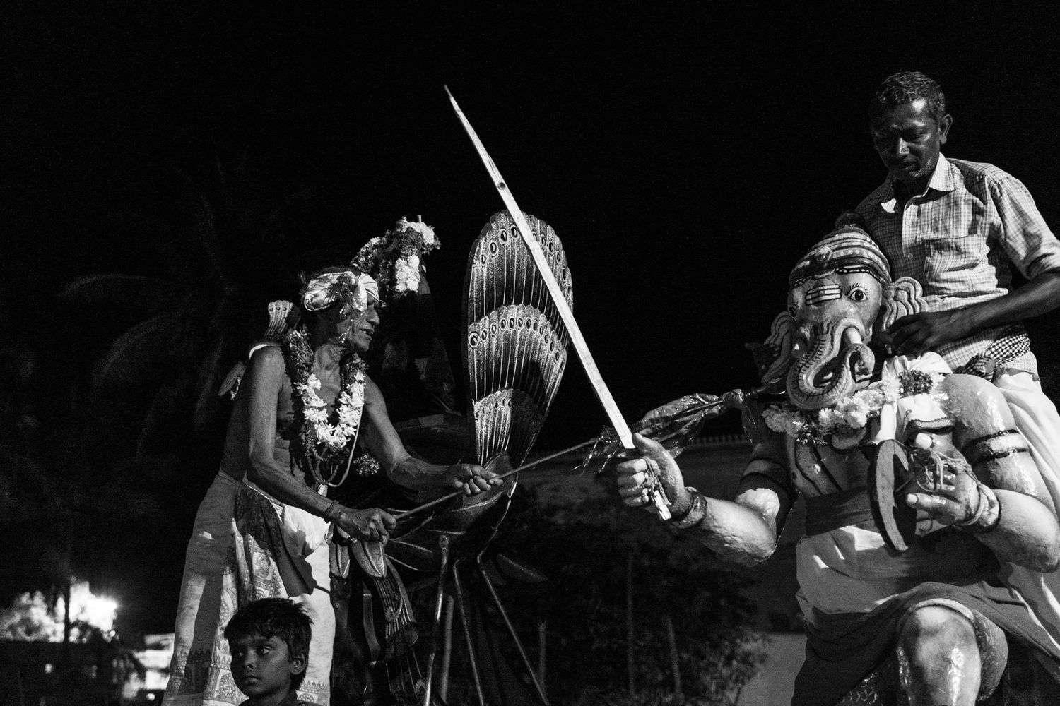 Traditional Hawaiian performers with ceremonial spears and kahili standards perform at night.