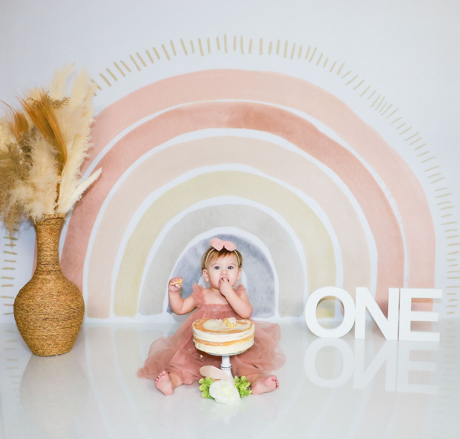 Pastel rainbow backdrop with 'ONE' text and baby-themed decorations for first birthday photography.