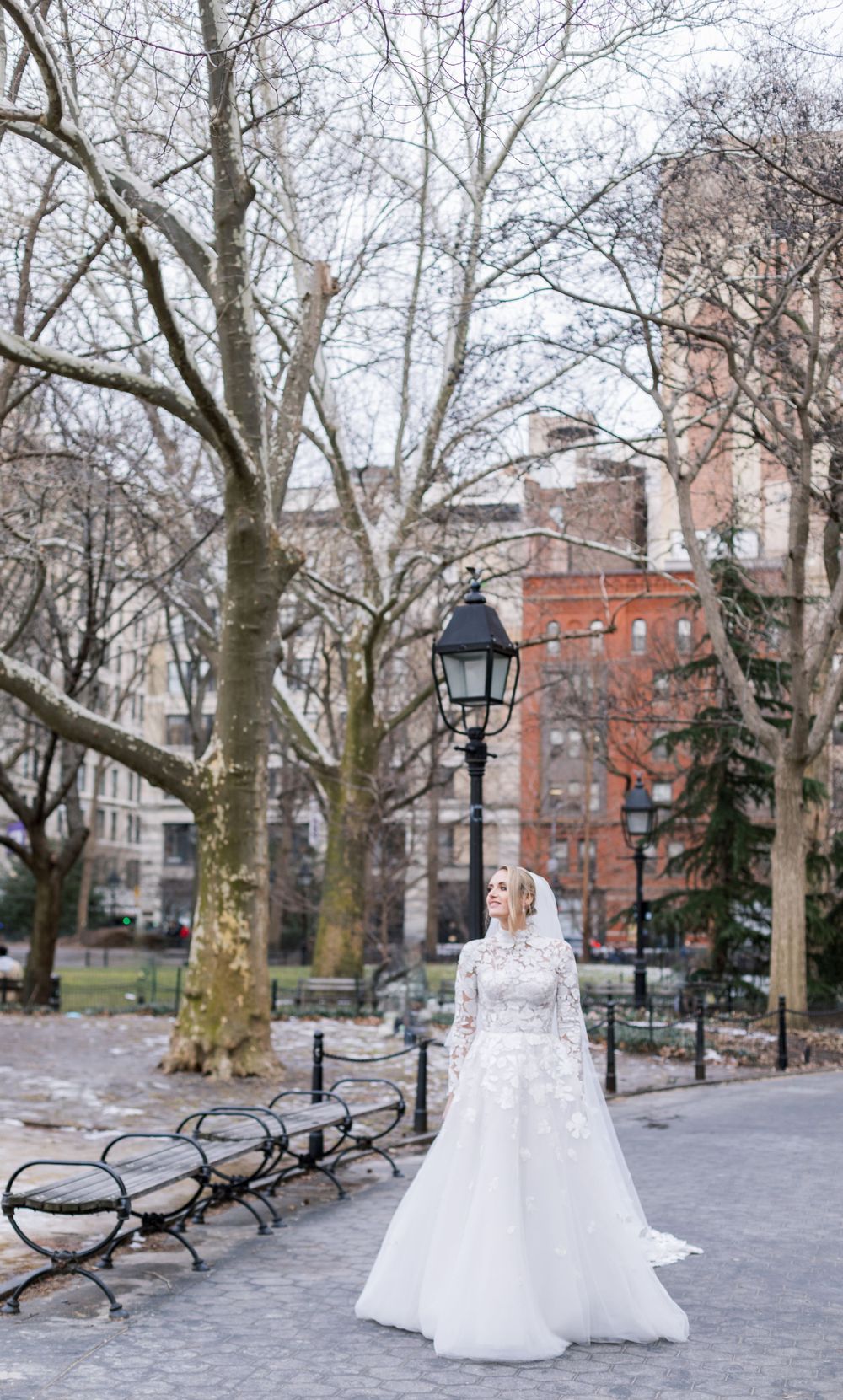 Winter wedding photo showing full bridal gown in Washington Square Park with bare trees.
