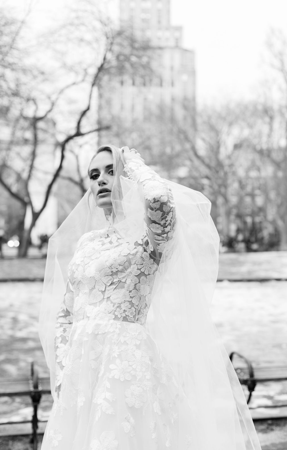 Artistic black and white bridal portrait showcasing a lace wedding dress and flowing veil in an outdoor setting.