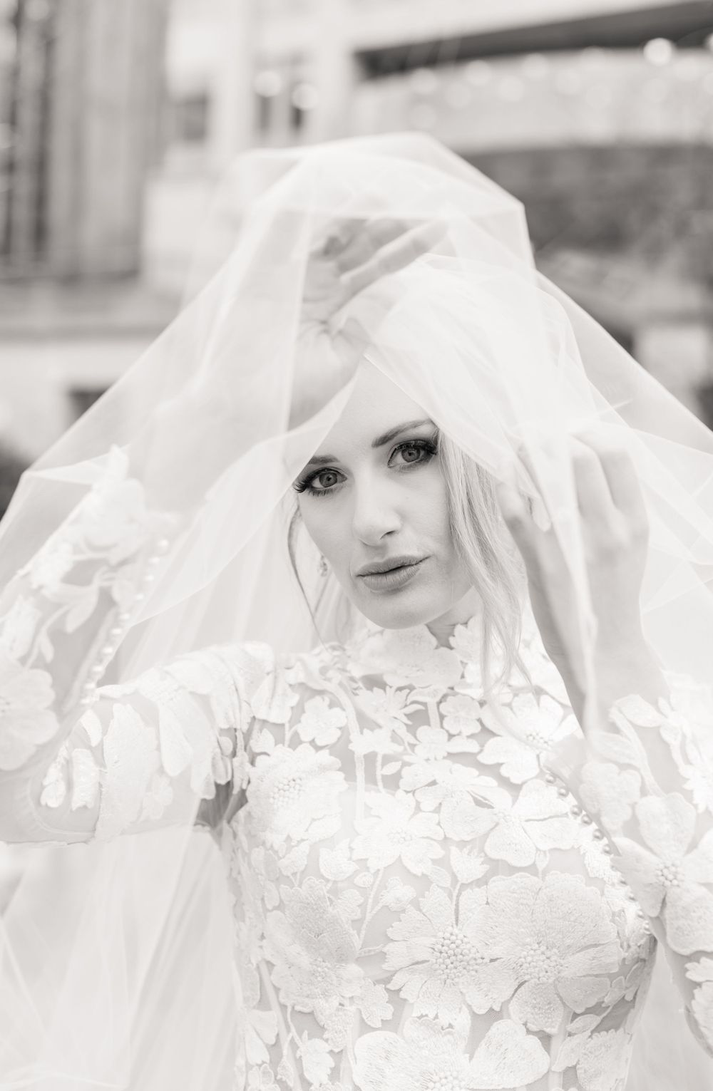 Black and white portrait of a bride wearing an intricate lace gown with flowing veil.