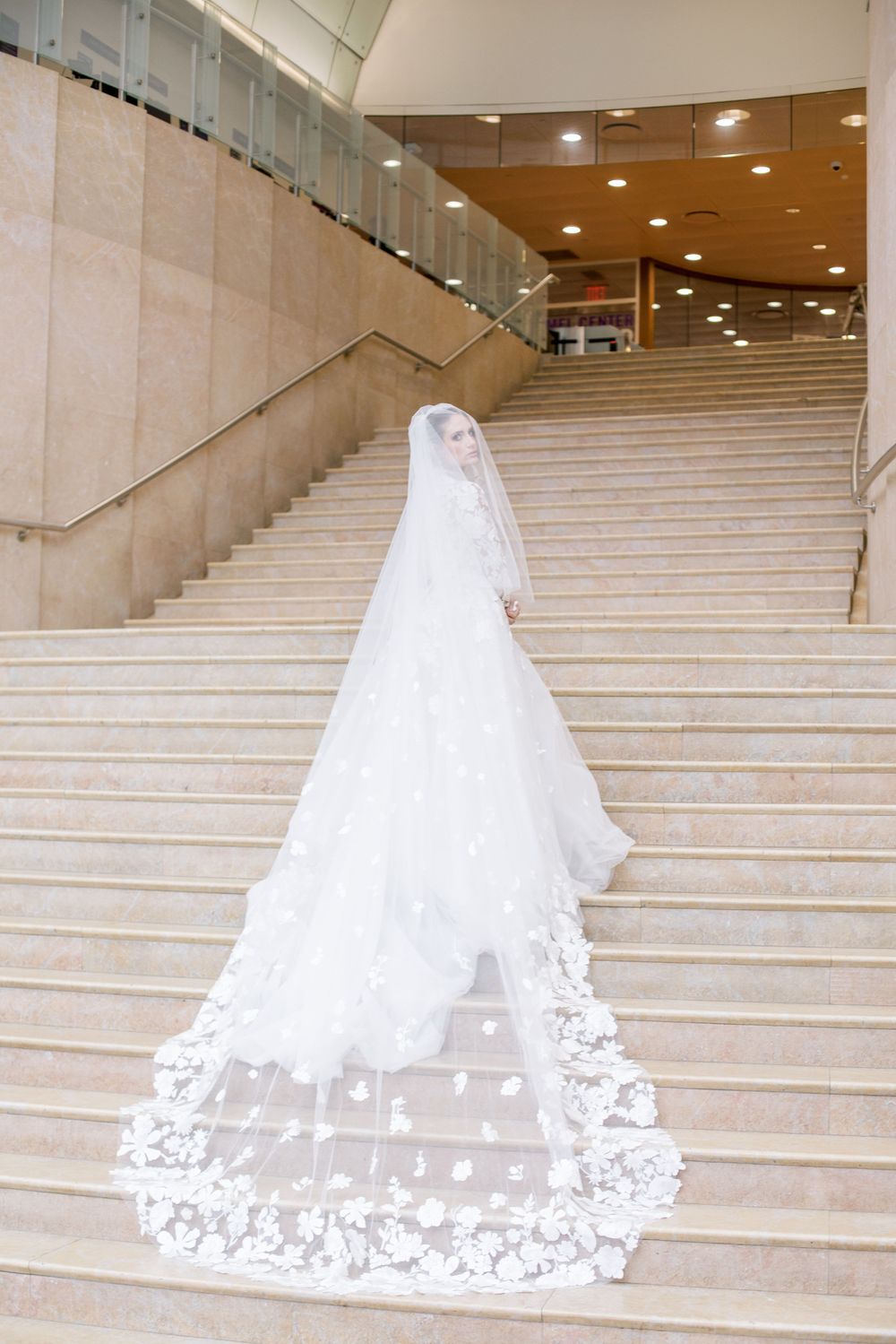 Wedding dress with cathedral length lace veil trailing down marble staircase.