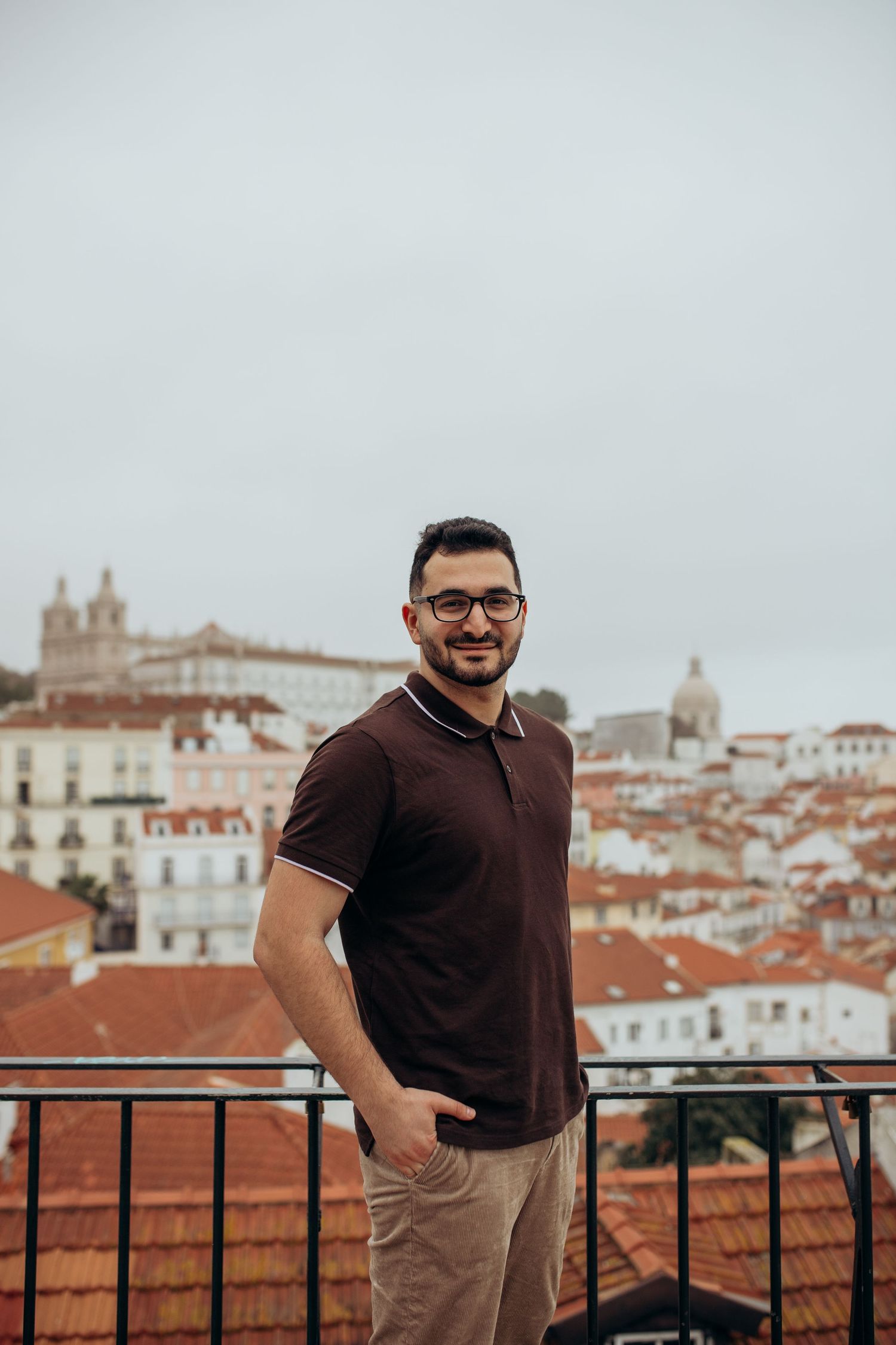 Person in casual attire enjoying a scenic view of Lisbon with historic architecture and terracotta rooftops in background.