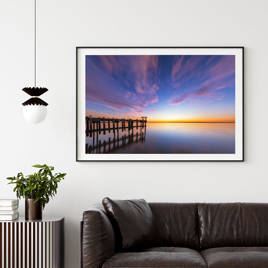 Framed pier photograph with dramatic sunset sky displayed in modern living room setting.