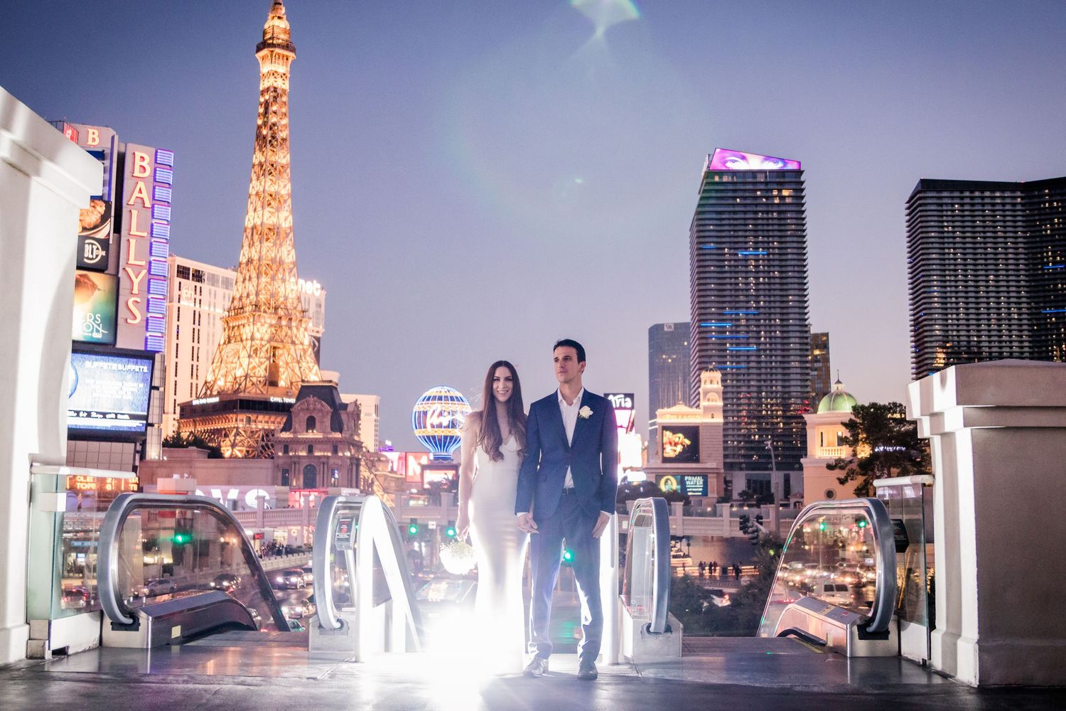 Silhouetted couple on rooftop with illuminated Paris Las Vegas hotel and city lights in background.