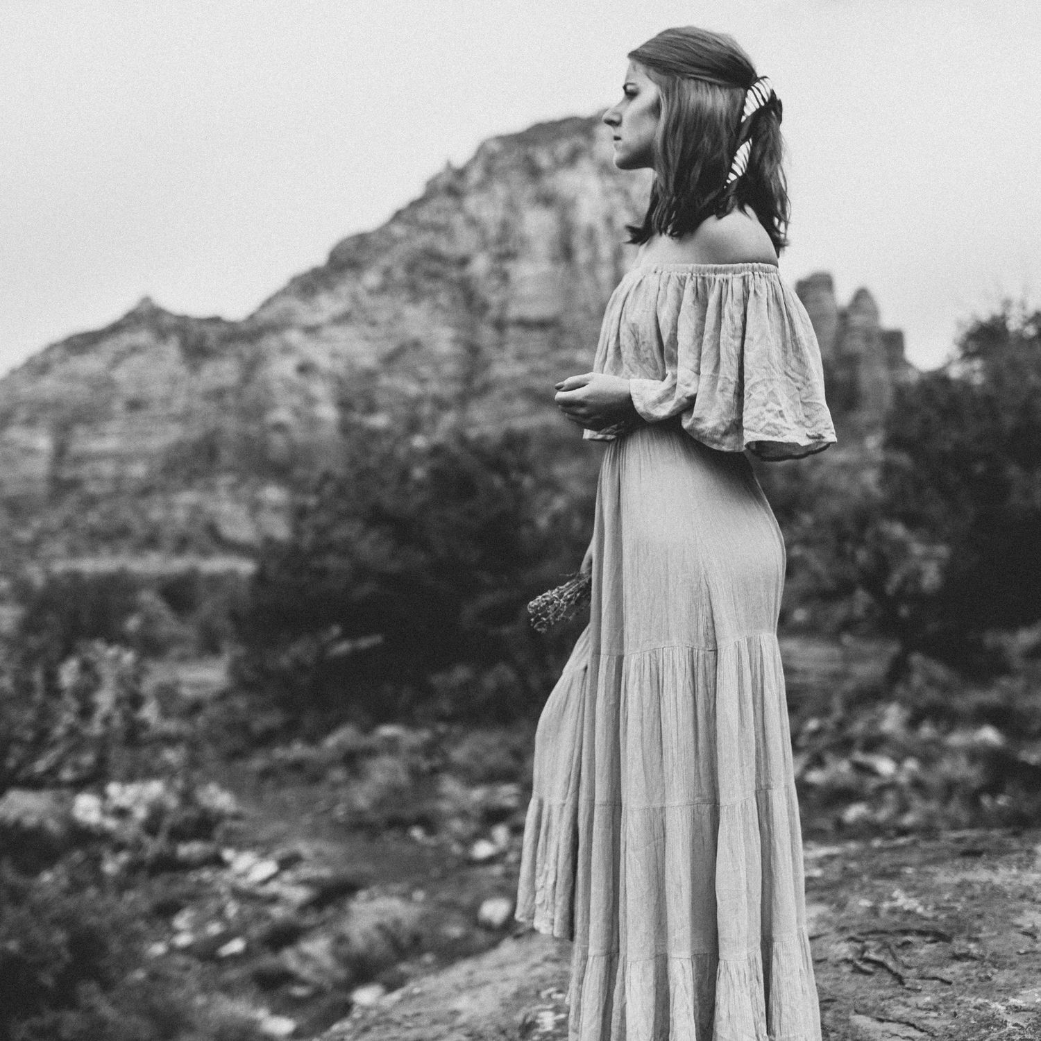 Person in vintage dress poses against mountainous backdrop in black and white photography.