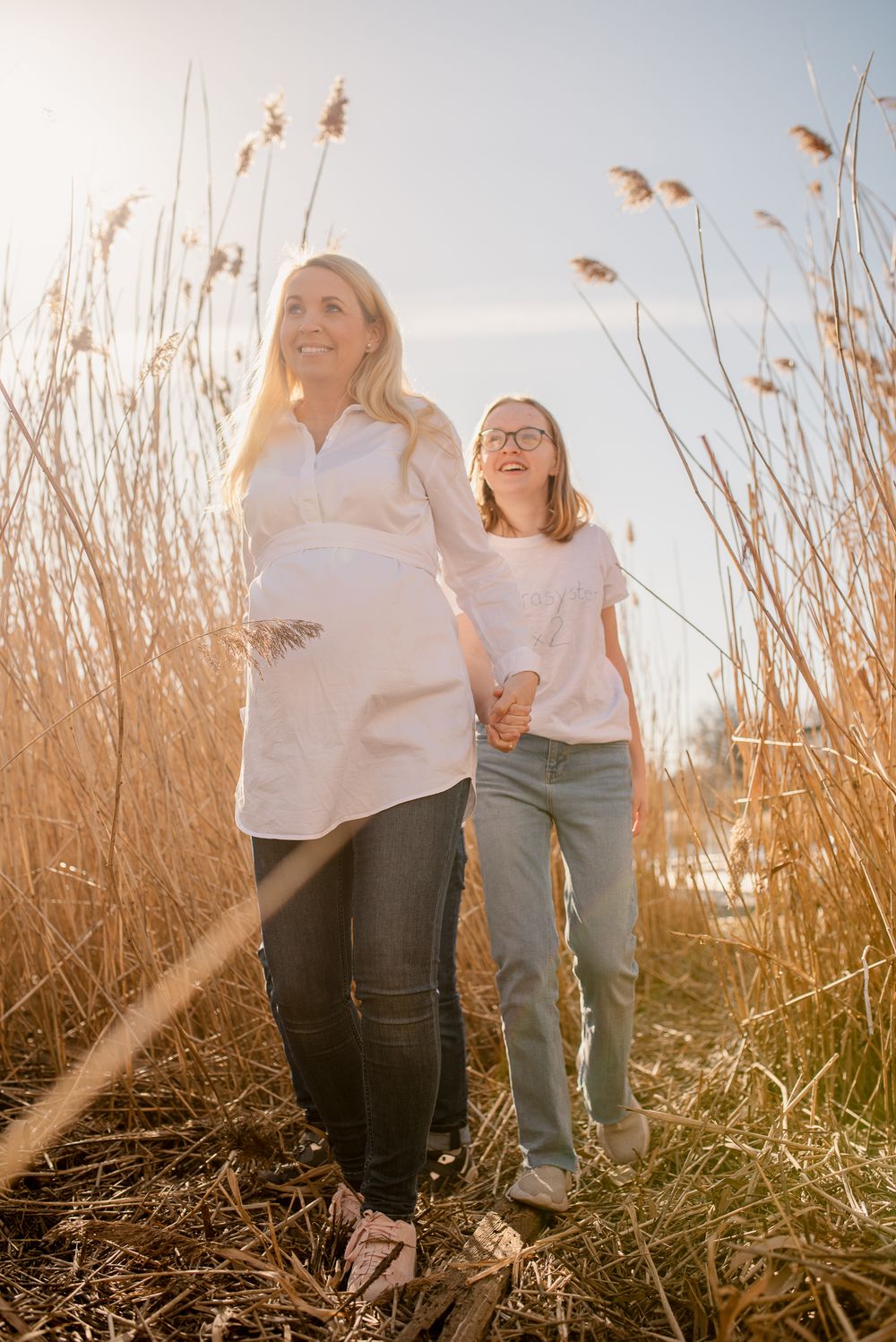 A joyful walk through tall golden reeds at sunset with coordinating white tops and casual denim outfits.