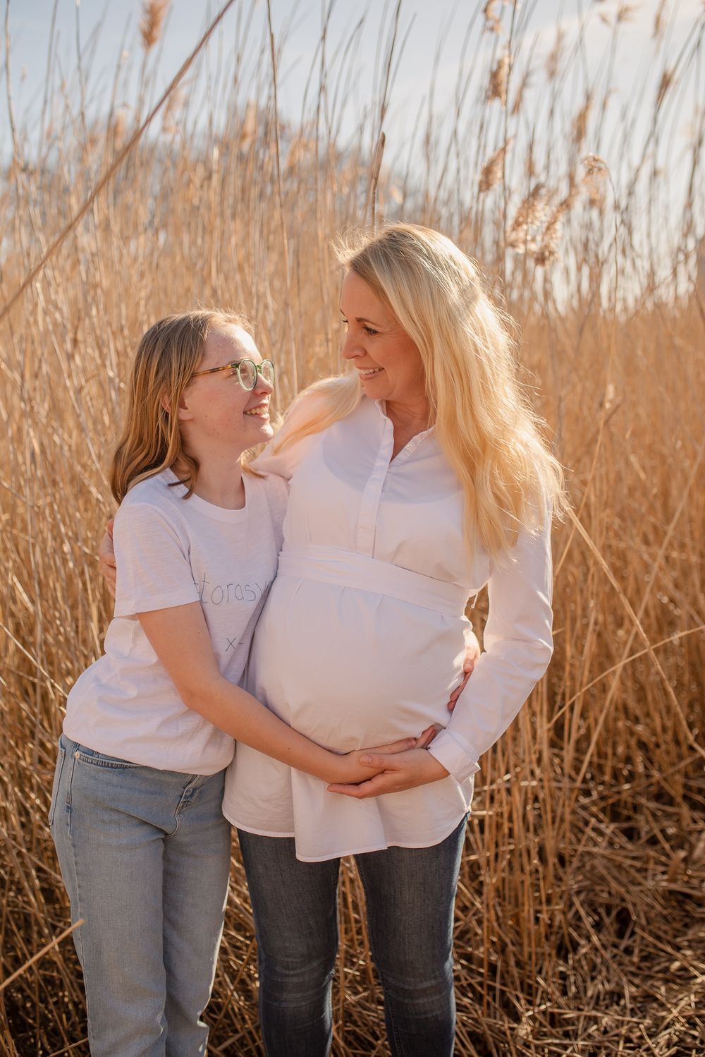 Tender moment captured amongst tall golden reeds during a maternity photoshoot.