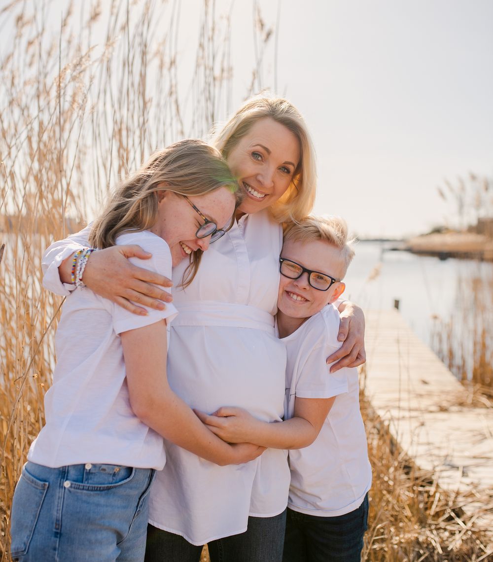 Family in white shirts embracing among coastal reeds at sunset.