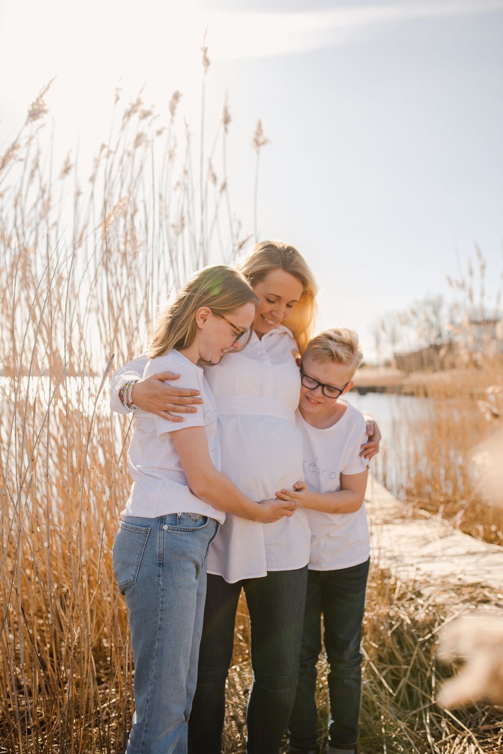 Family sharing tender moment among tall reeds by waterfront.