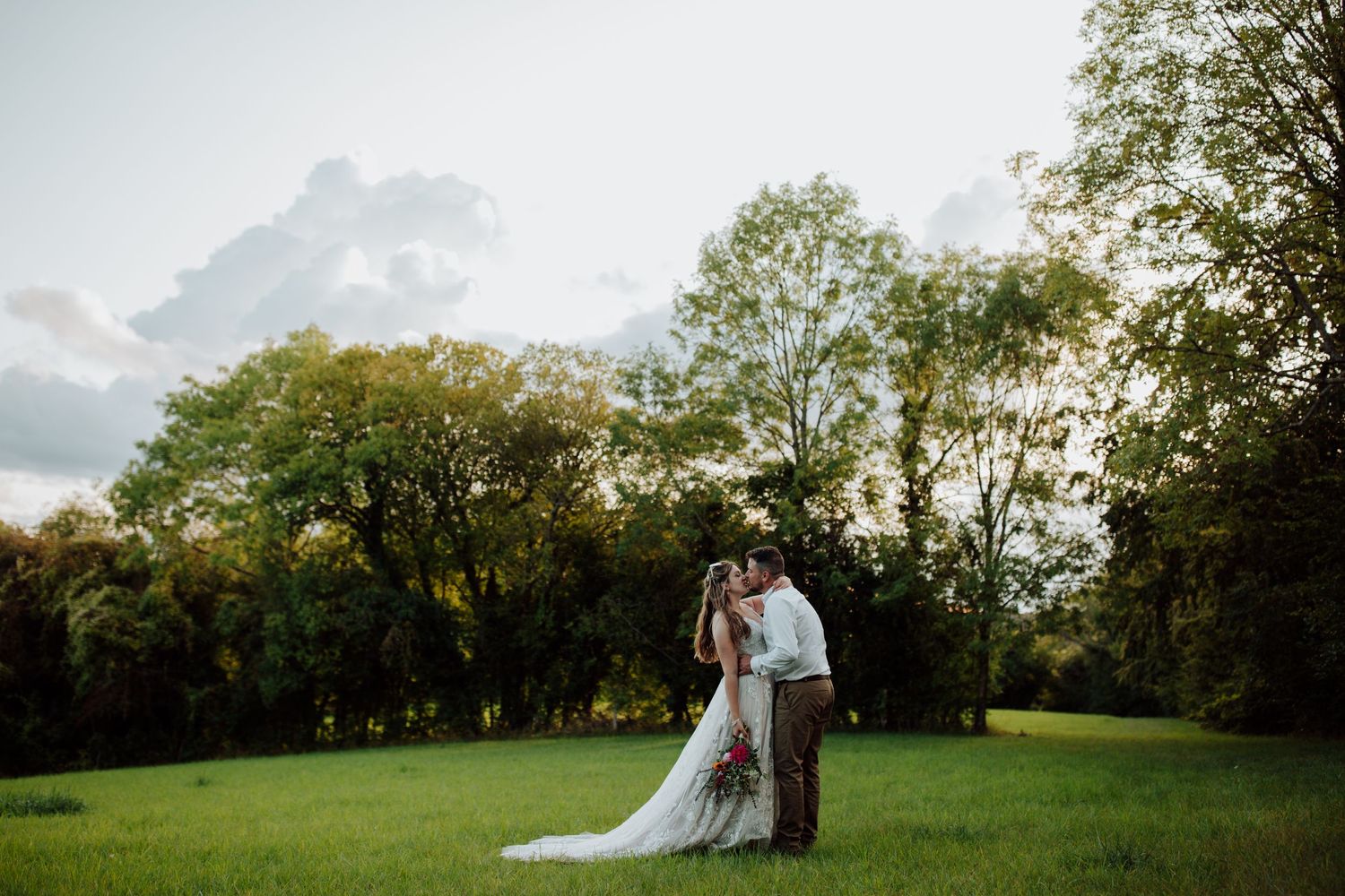 A couple stands together on a grassy hill during golden hour wedding photography.