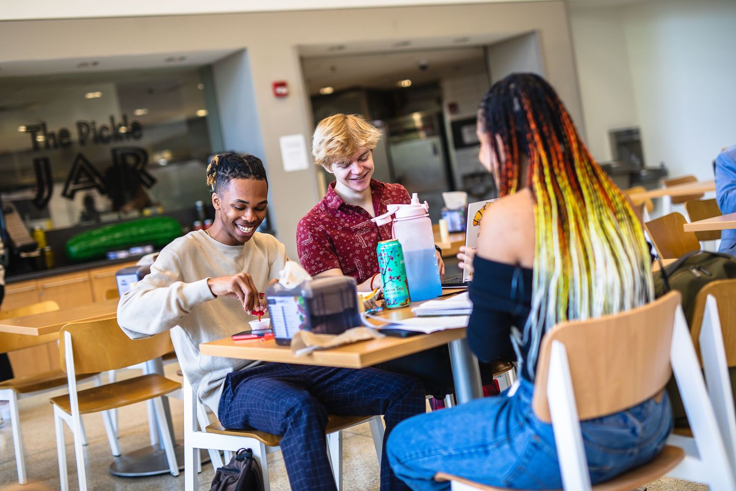 Students enjoying lunch and conversation at a table in a casual cafeteria setting.