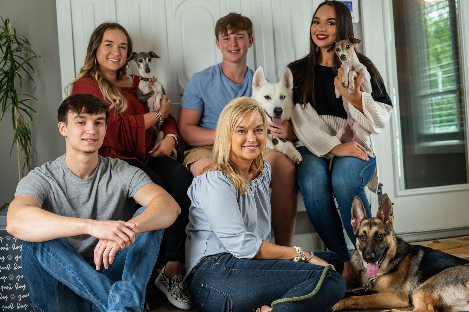 A casual indoor group photo featuring several people and their pets including a white dog and German Shepherd.