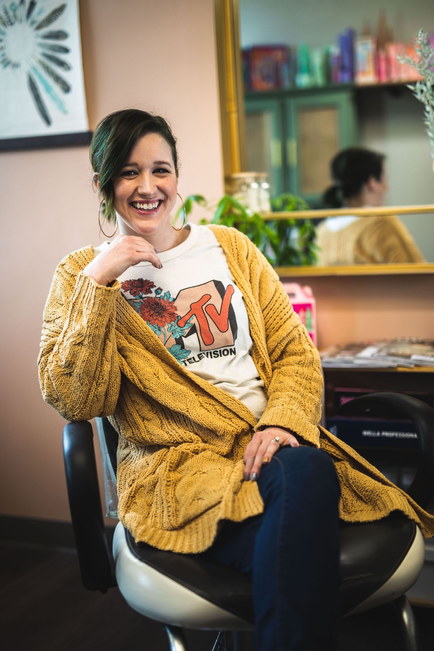 A person wearing a yellow cardigan and graphic t-shirt sits in a modern office setting.