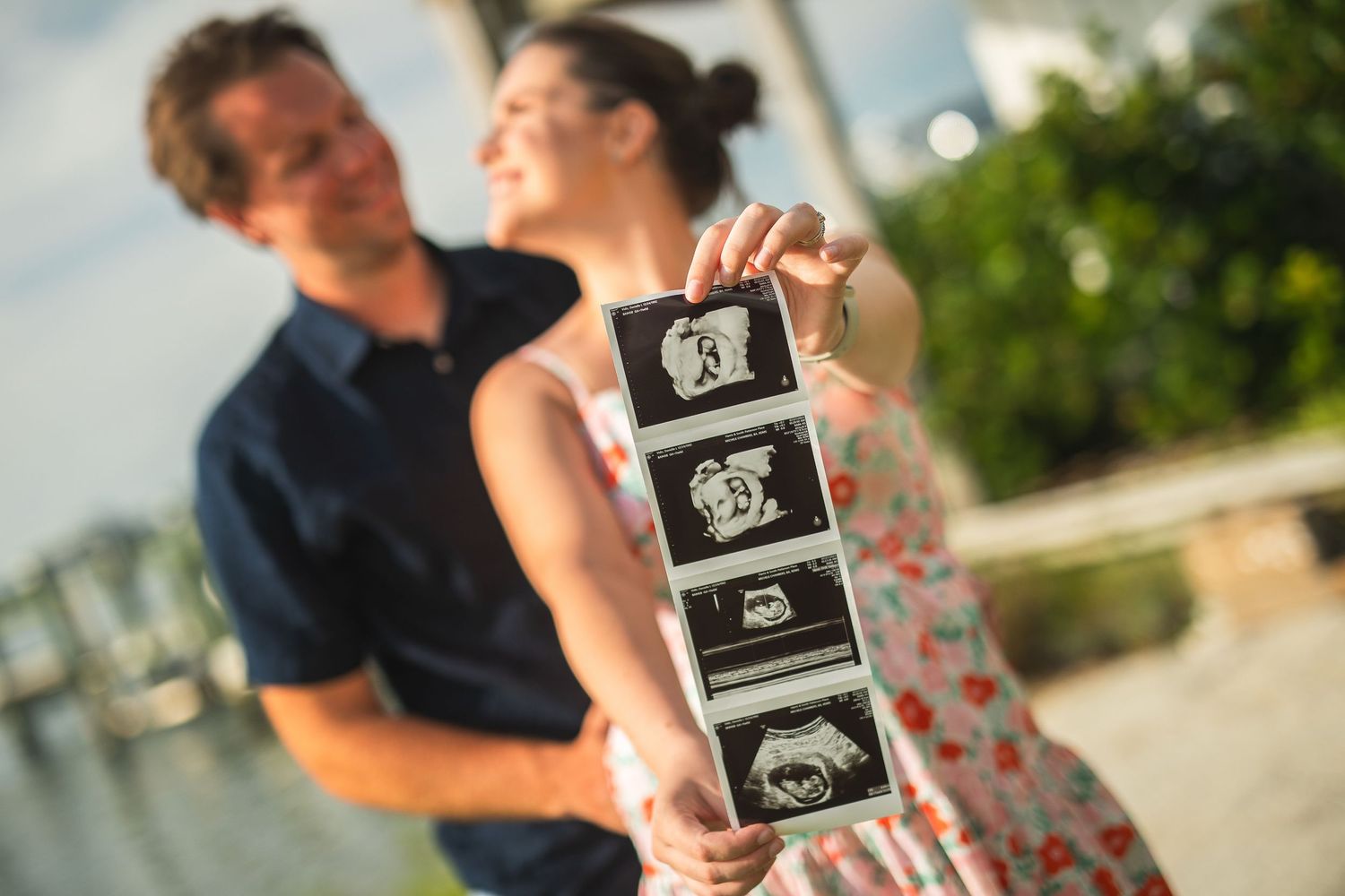 A couple holding ultrasound photos outdoors during a pregnancy announcement photoshoot.