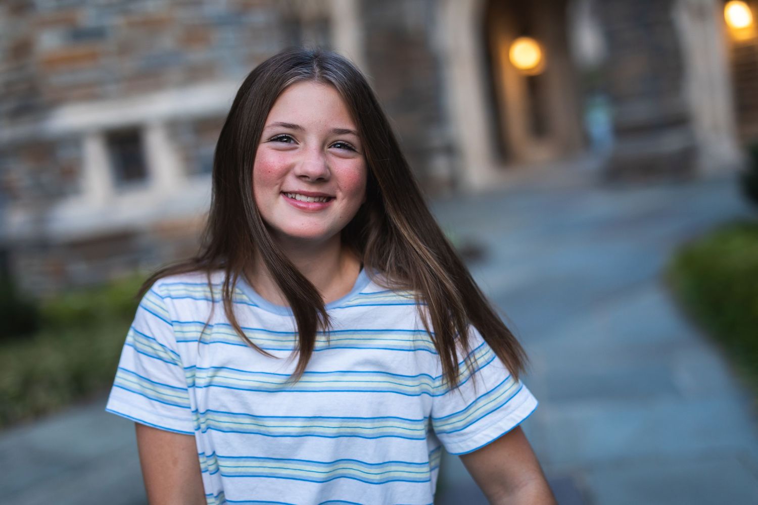 A casual outdoor portrait with stone architecture and evening lighting in the background.