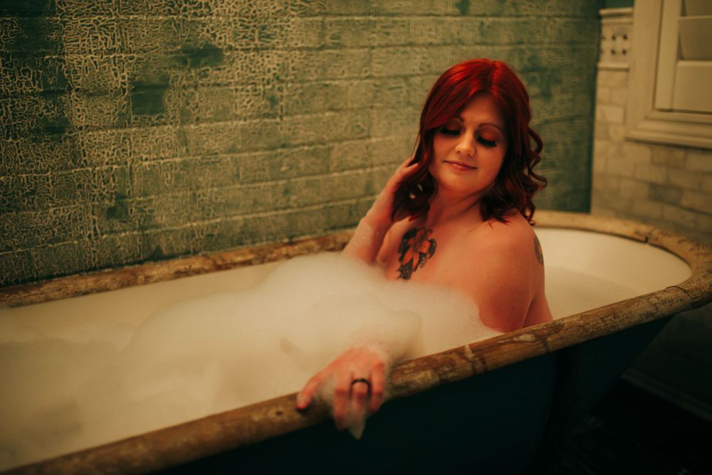 Woman with red hair relaxes in vintage clawfoot bathtub filled with bubbles.