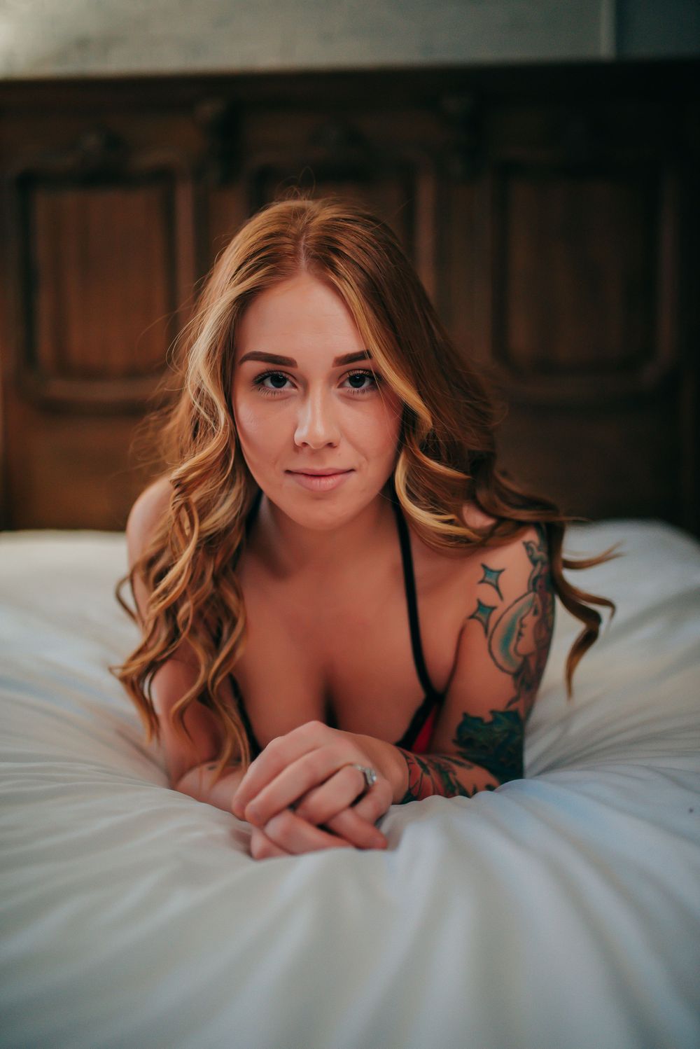 Intimate boudoir photograph in warm tones with soft lighting and bedroom setting.