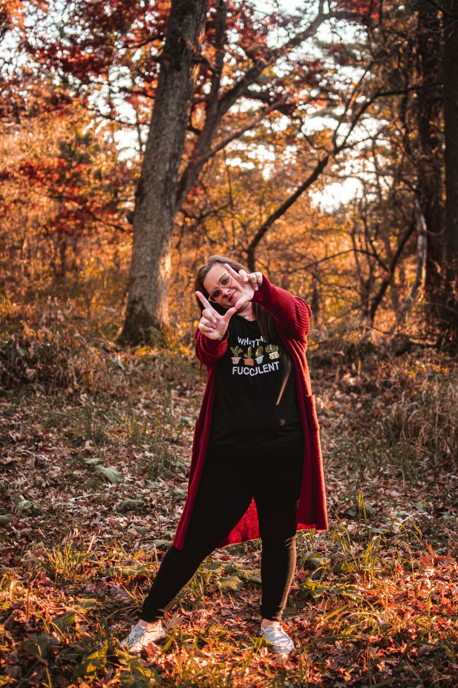 Person striking a fun pose in a red cardigan among fall foliage.