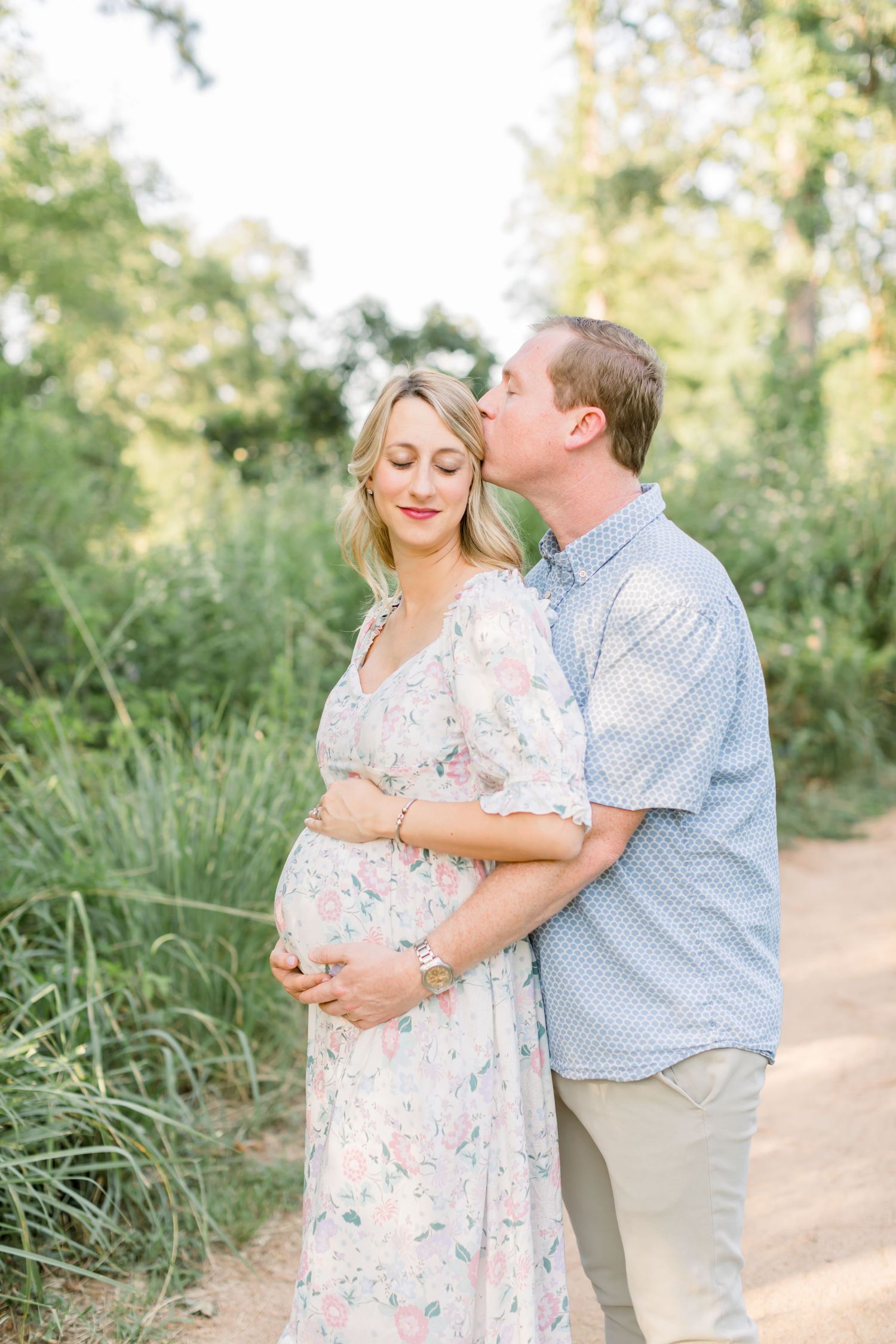 A tender moment between expectant parents on a nature path during golden hour.