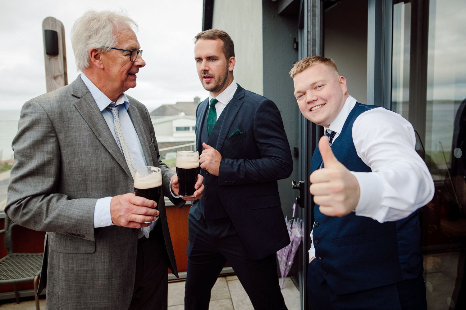 Three wedding guests enjoy drinks and conversation on an outdoor patio.