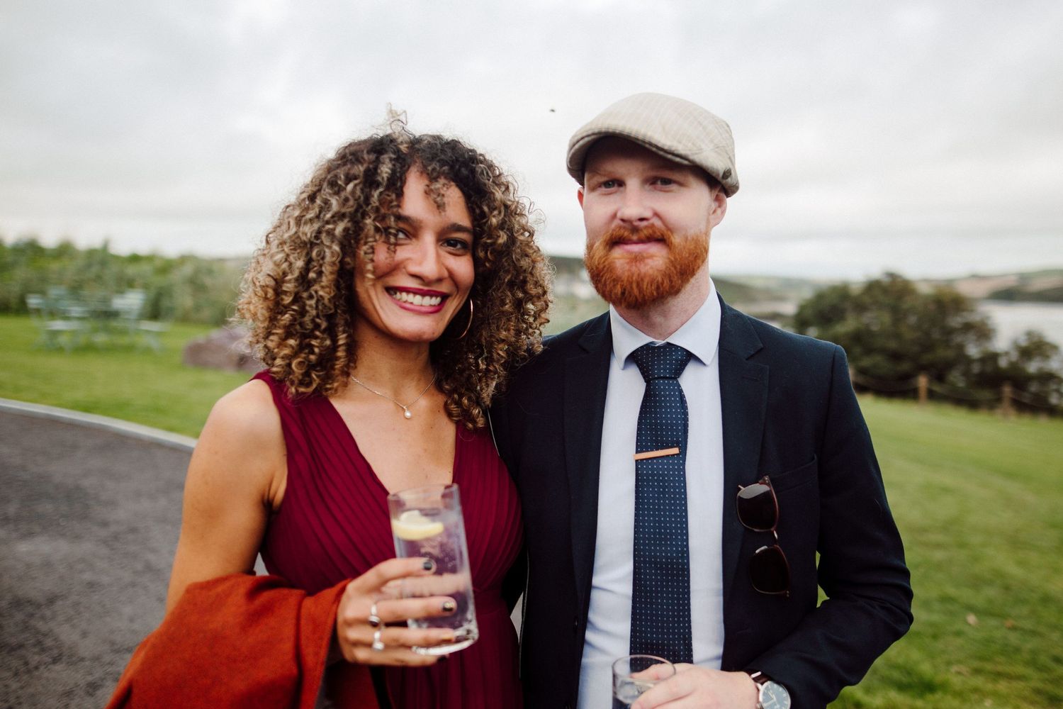 A couple enjoys drinks at an outdoor wedding reception with coastal views.