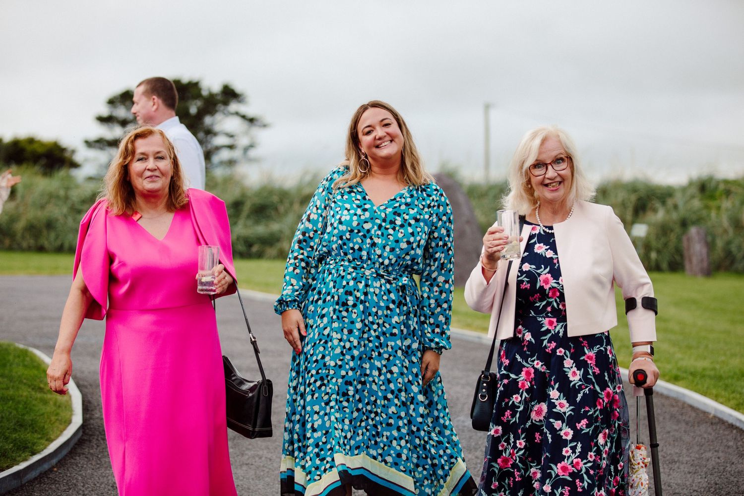 Three friends in colorful dresses laugh and smile together outdoors on a cloudy day.