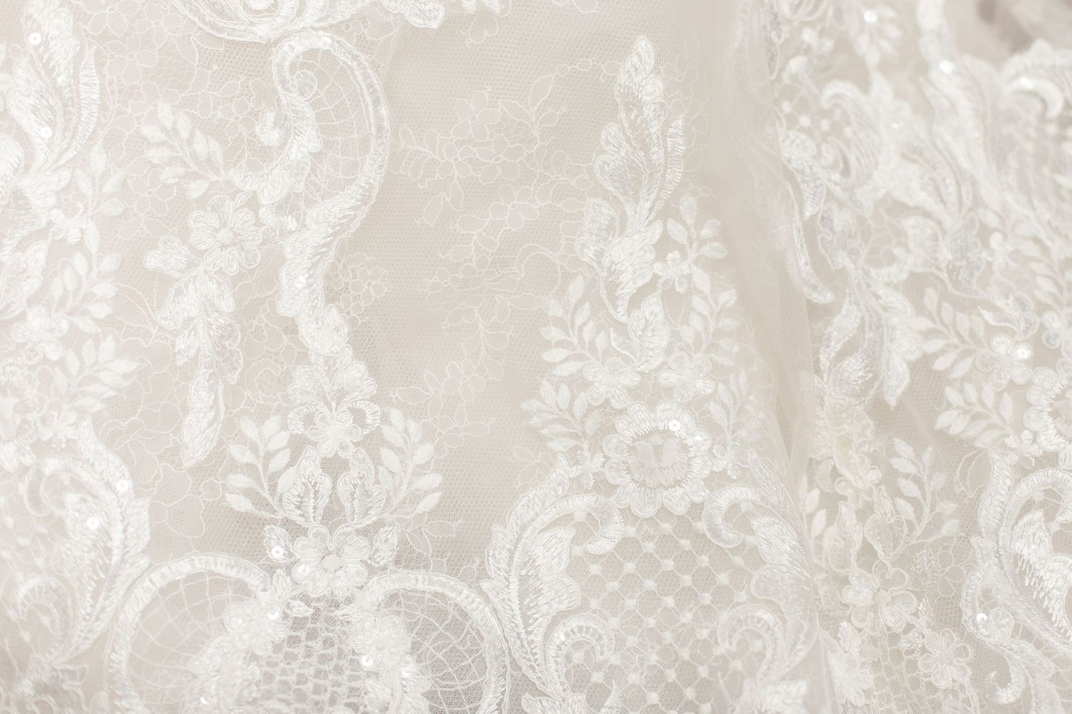 Detailed view of white lace embroidery pattern on wedding dress fabric.