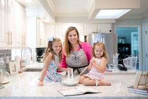 Three people baking together in bright modern kitchen with marble countertops.