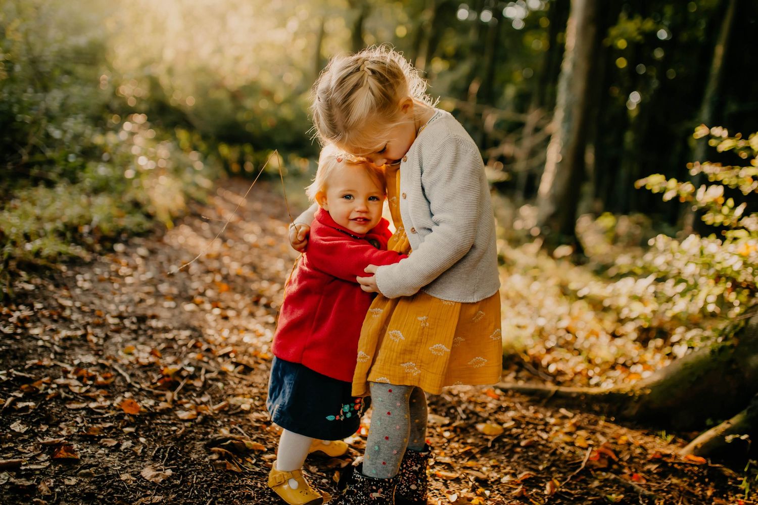 Two little sisters standing together and hugging in a sunlit forest