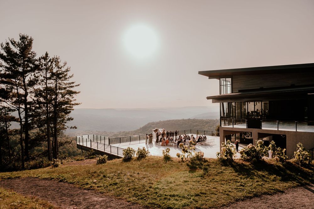 A misty sunset view from a mountaintop venue overlooking a scenic landscape as guests gather on a spacious outdoor deck.