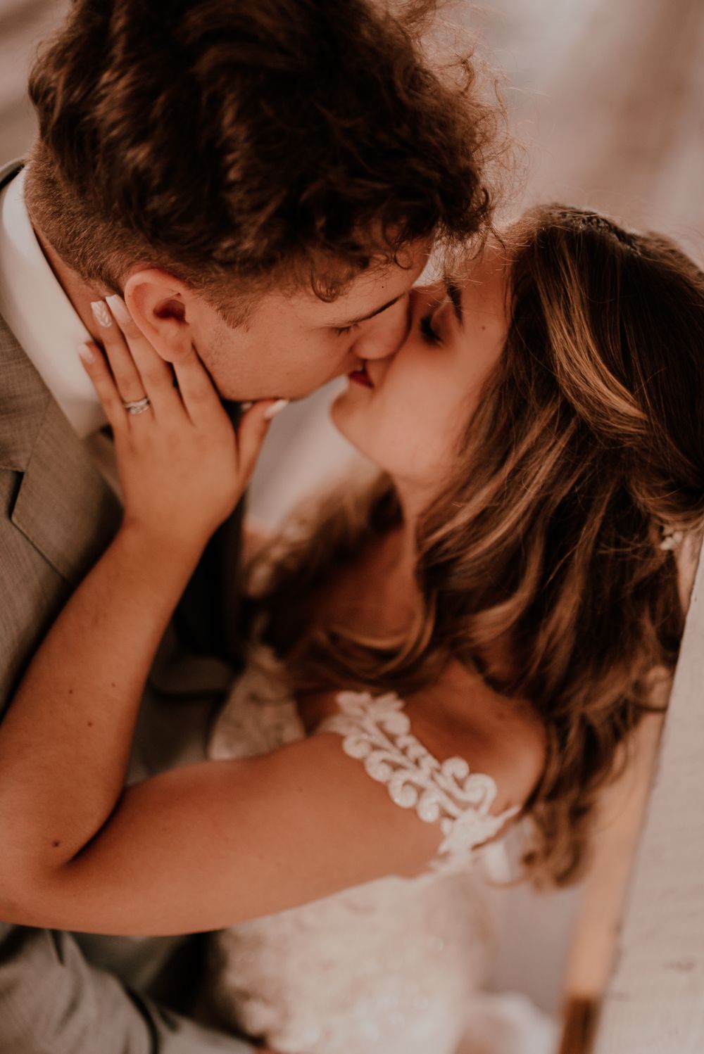 A romantic close-up photo of a couple kissing on their wedding day captured in warm sepia tones.