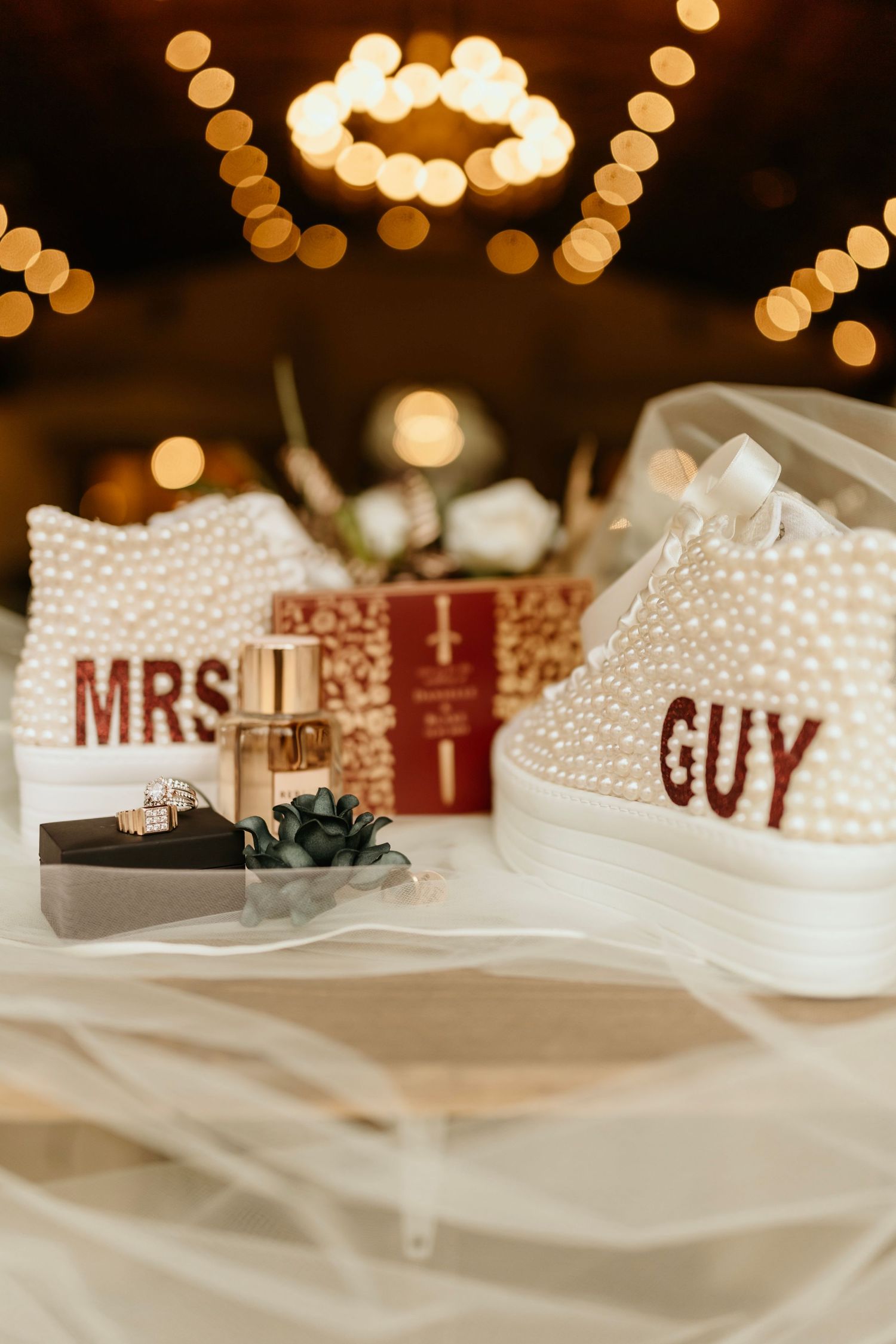 Decorated wedding sneakers with 'MRS' and 'GUY' text displayed with rings and bokeh lighting.