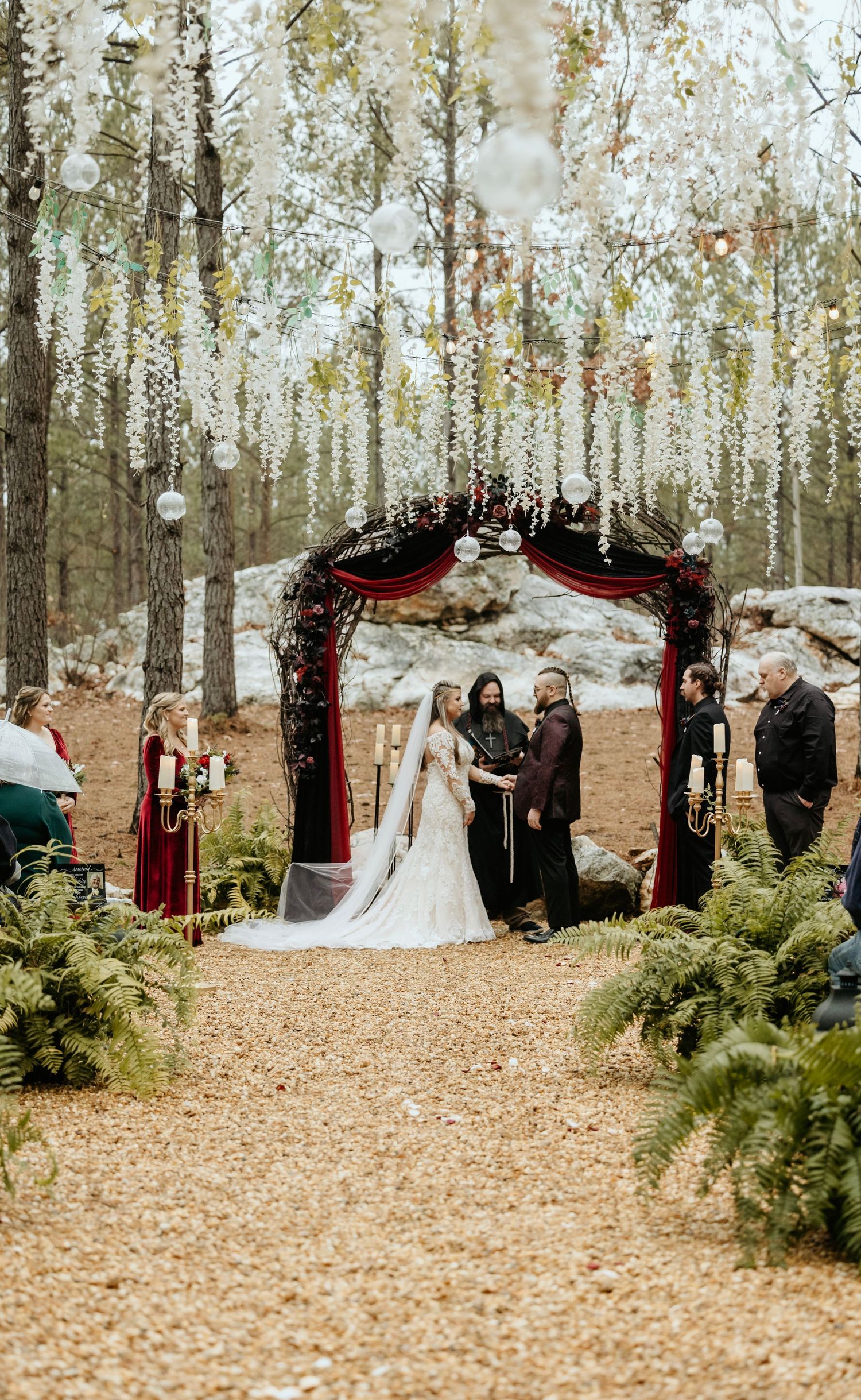 Outdoor winter wedding ceremony under hanging white wisteria and red arch decor.